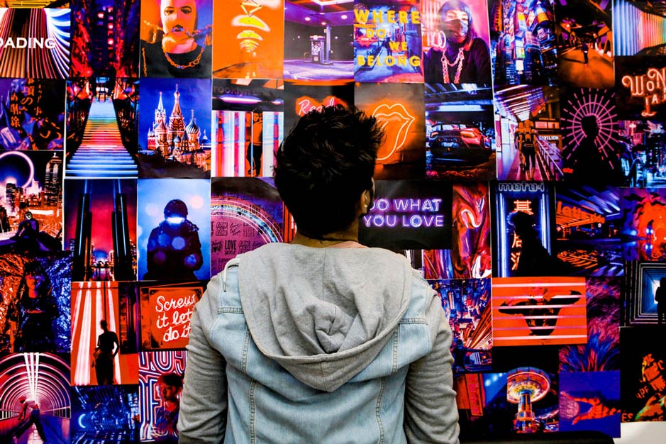 guy looking at a wall with trippy neon posters collage