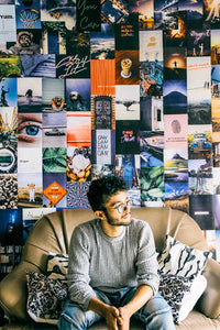 A young man sitting on a couch with aesthetic collage kit posters behind on the wall