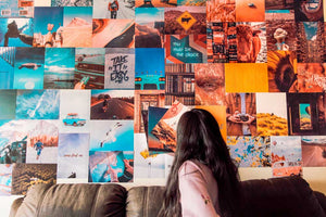 Girl putting up colorful travel posters collage on a wall over a black couch