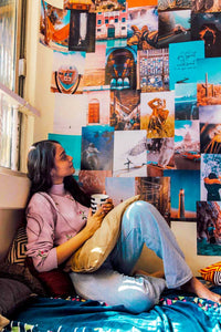 A young lady admiring her wall of travel posters collage while sipping her coffee